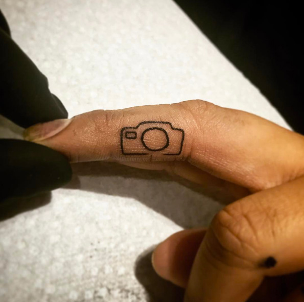 Tiny camera tattoo on finger by Savage Sal