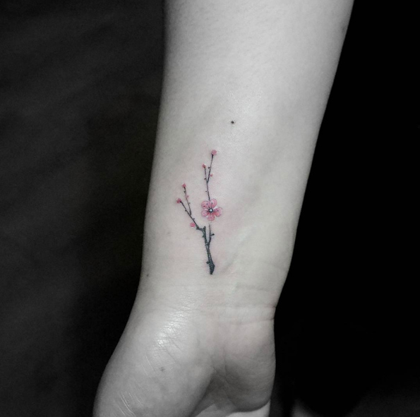 Tiny cherry blossom tattoo on wrist by Tattoo With Me